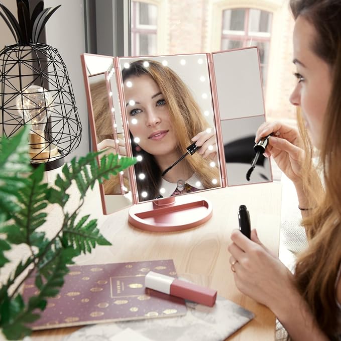 A woman gazes into a tri-fold makeup mirror with LED lights, featuring 1x/2x/3x magnification for a clear view of her reflection