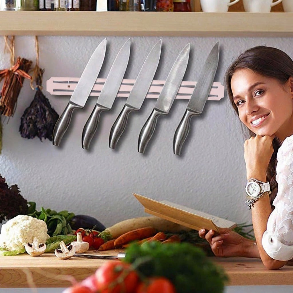 A wall-mounted magnetic strip holding multiple kitchen knives neatly in a row, placed above a kitchen counter where vegetables are prepared, with a person sitting nearby.