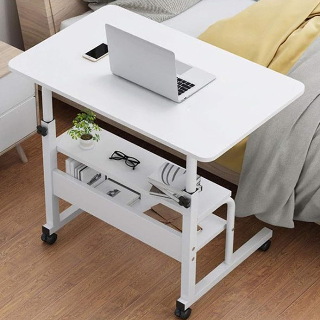 Adjustable Laptop Computer Desk with Bottom Shelf Placed Near Bed.