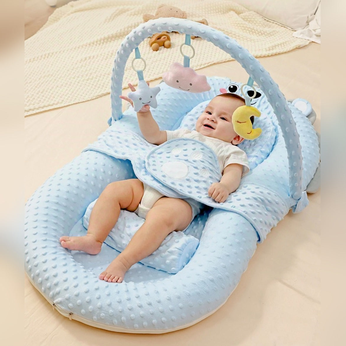 A Baby is Lying Down and Playing on the Comfortable Baby Nest Bed.