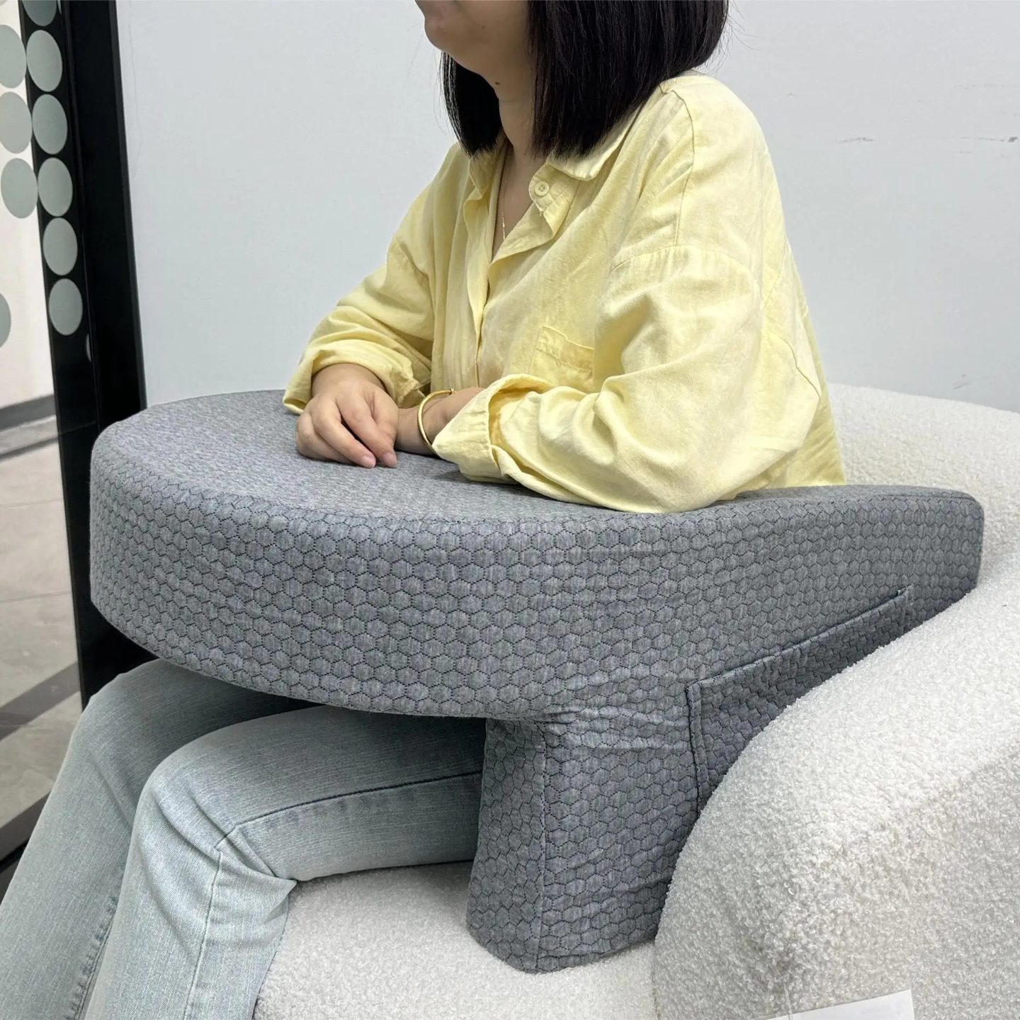 A Women is Sitting On a Sofa with the Aid f Bed Reading Pillow.