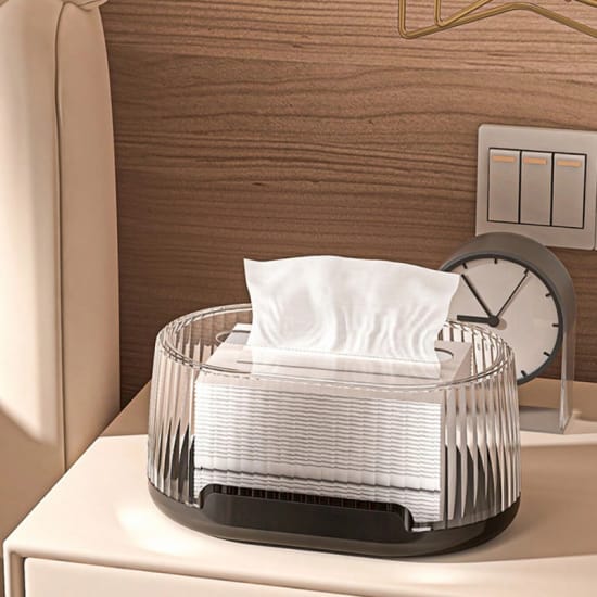 Black Oval shaped transparent tissue box is placed on the table,with one tissue pulled up and ready for use.