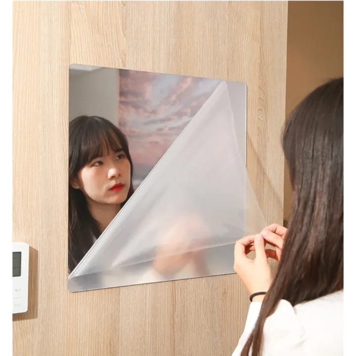 A woman carefully securing an HD Self-Adhesive Acrylic Mirror with tape for installation