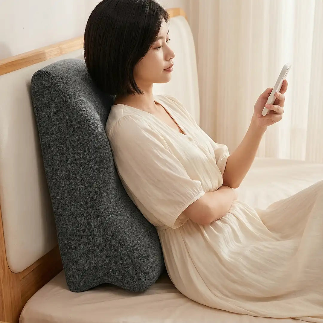 A woman using a smartphone with a Green Lion Relief Wedge Pillow against her back on a bed.