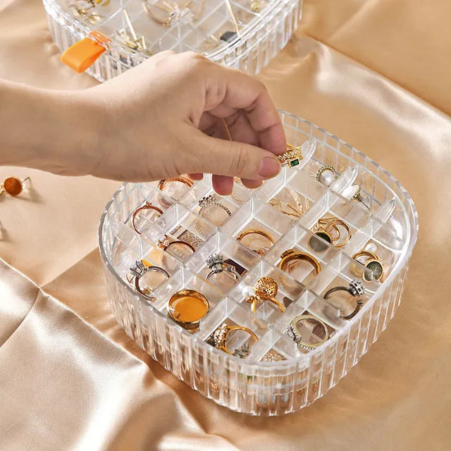 A cosmetic and jewelry storage box with a lid, containing rings and earrings neatly organized inside.