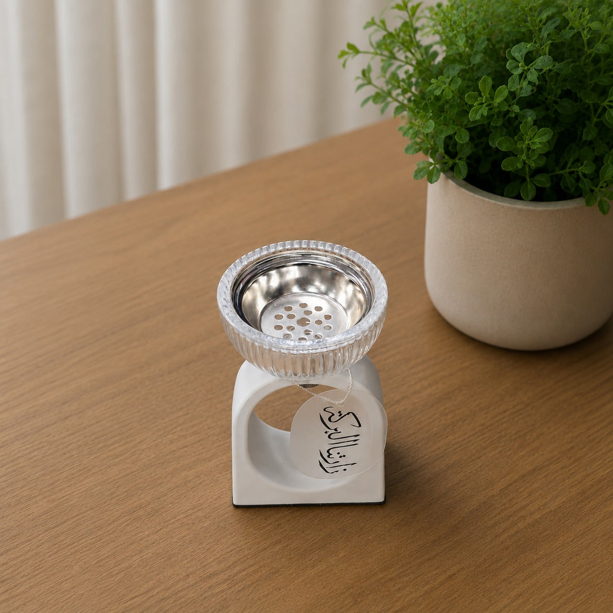 Incense burner with metal top on a wooden surface next to a potted plant.