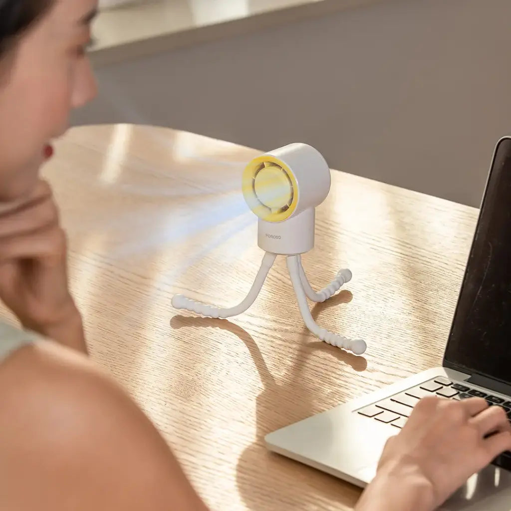 Person using a laptop with Porodo CoolFlex Mini Handheld Fan on a wooden desk
