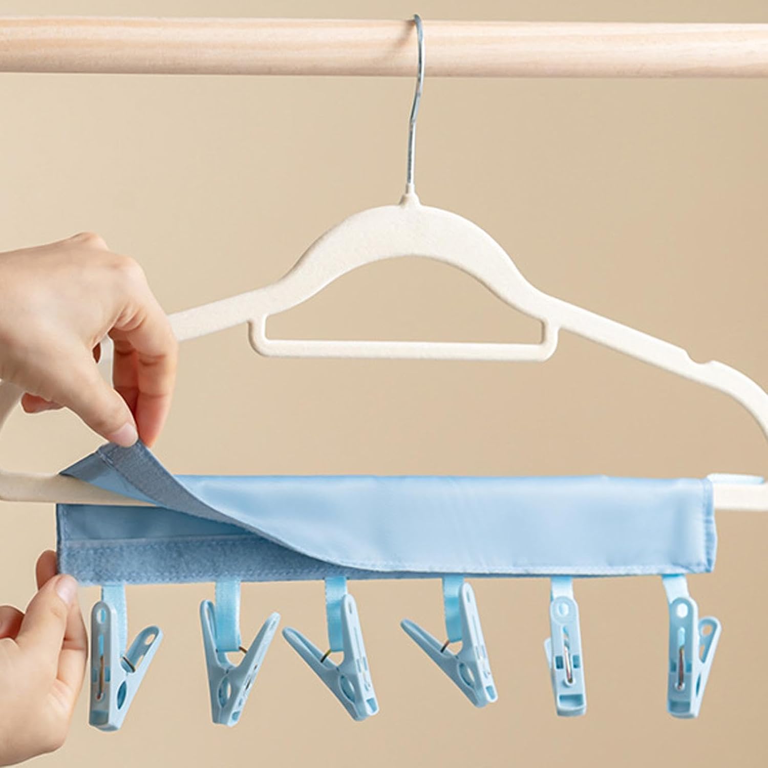 A person adjusting a multi-clip hanger with a soft blue fabric cover, attached to a standard clothes hanger.