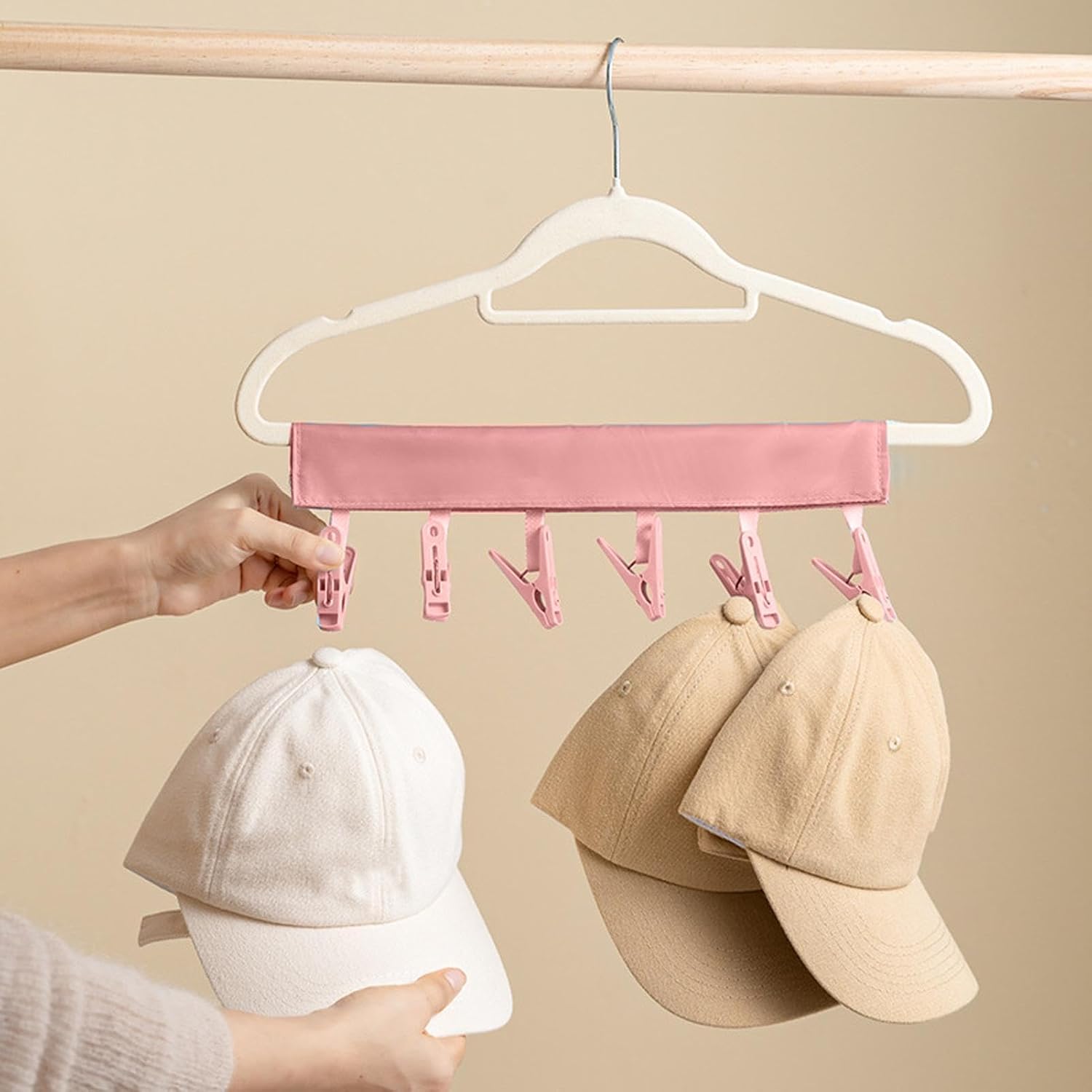 A person using a pink color multi-clip hanger to hang baseball caps attached to a cloth hanger