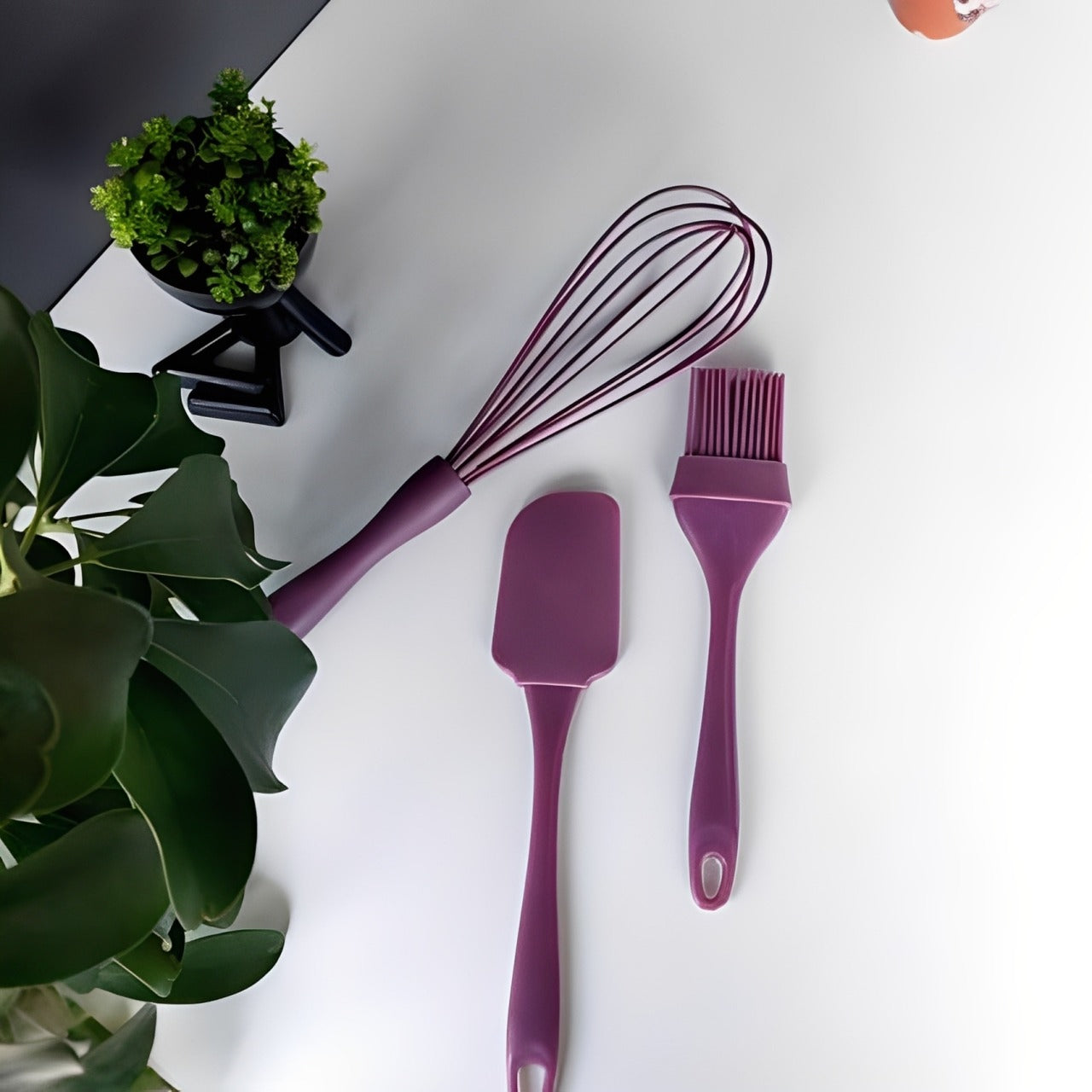 A brush and spatula placed on a white floor, surrounded by green leaves.