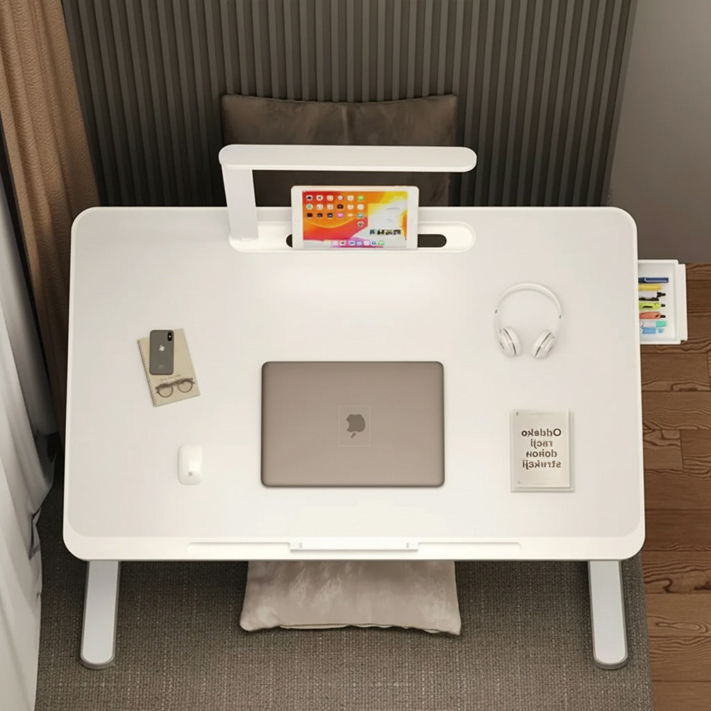 Portable foldable laptop bed desk table with adjustable legs and built-in LED lamp, arranged with laptop and other essentials.