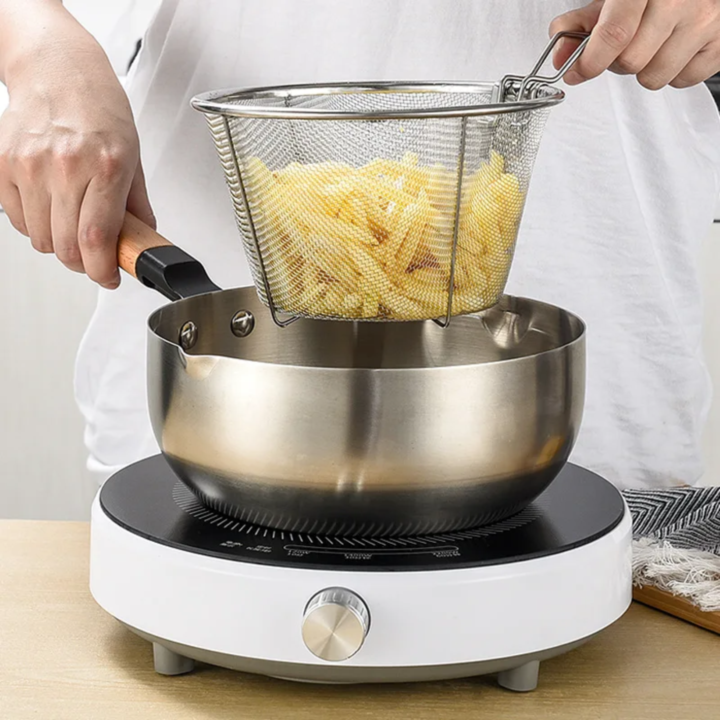 A person using a Stainless steel mesh basket for straining cooked pasta over a pot on an induction cooker