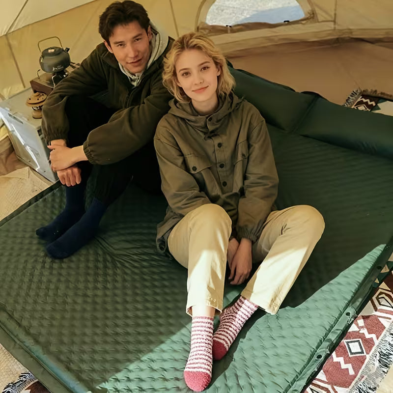 Couple sitting inside a camping tent on a green self-inflating camping mattress with built-in pillow.