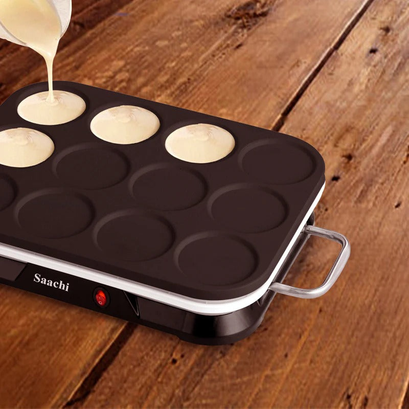 A Saachi electric pancake maker placed on a wooden surface, with batter being poured into the molds for making mini pancakes