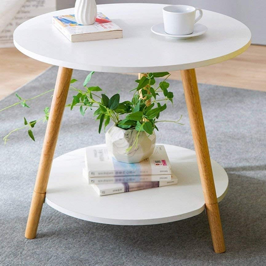 Round white table with wooden legs, holding a cup, vase, and books; plant and more books on the lower shelf.