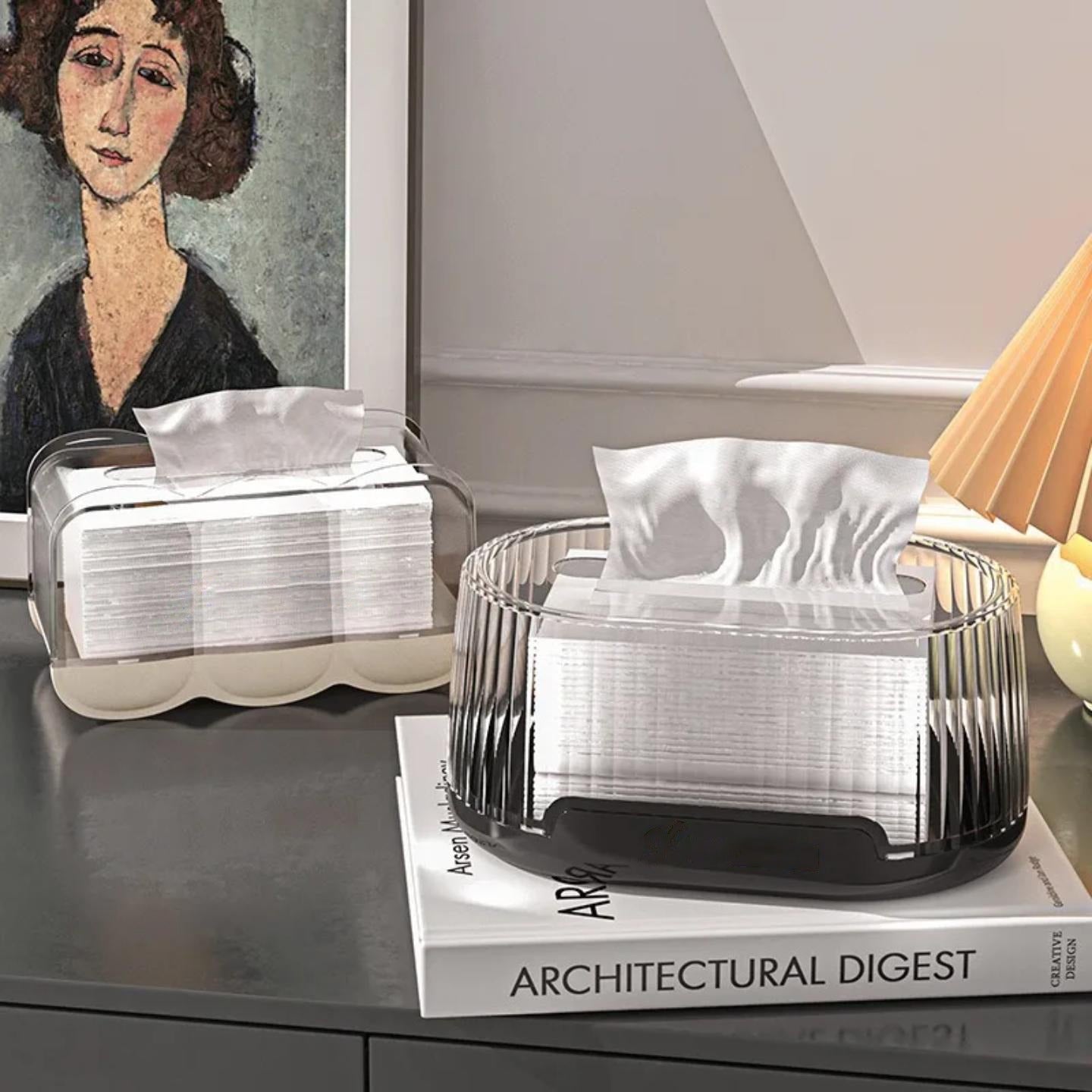 The wave shaped transparent tissue box on a table and oval shaped transparent tissue box on top of books.