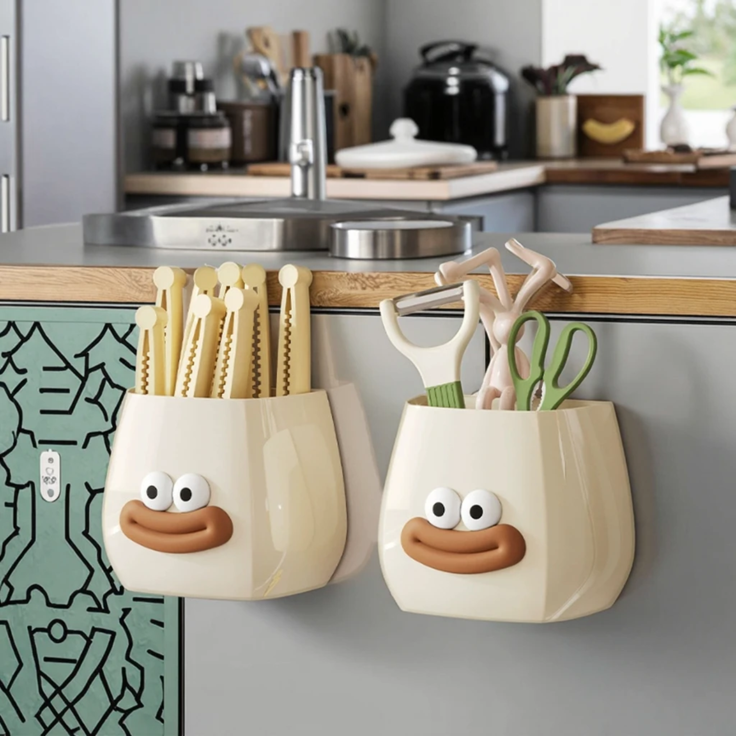 Two cute cartoon-style wall-mounted organizers with smiling faces, used to store kitchen tools like peelers, scissors, and utensils while adding a fun decorative touch.