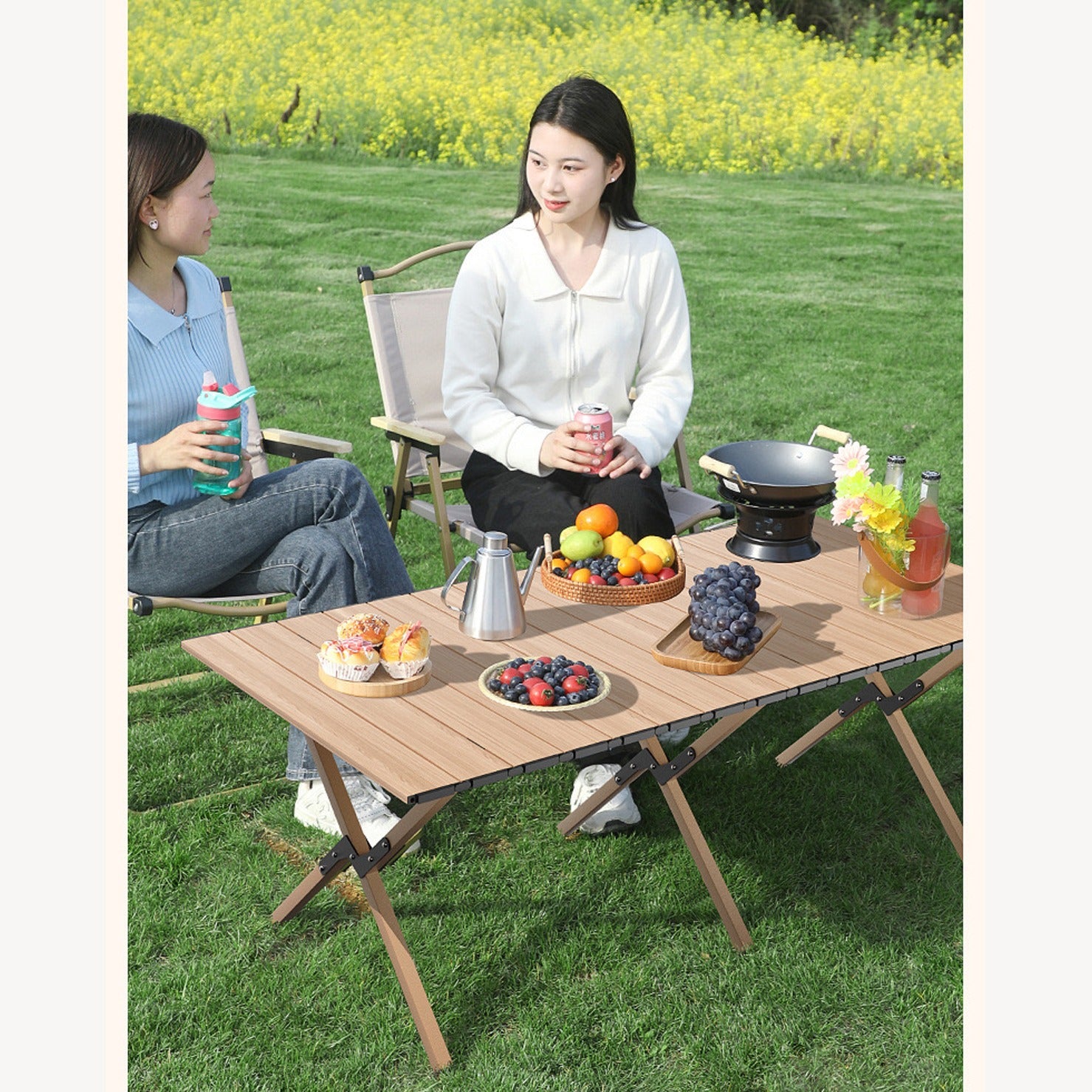Outdoor Portable Camping Table and chair with fruits,snacks and drinks placed on top of it being used by two ladies in a picnic at a park