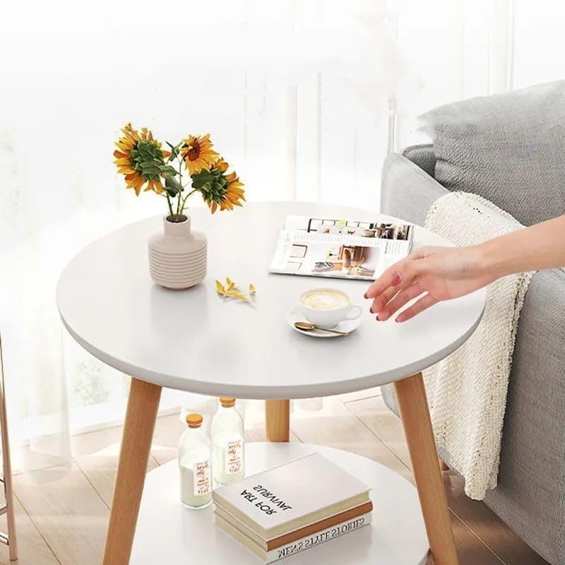 A round side table is placed in a cozy living room. On the tabletop are a vase of sunflowers, a magazine, and a person taking a cup of coffee.