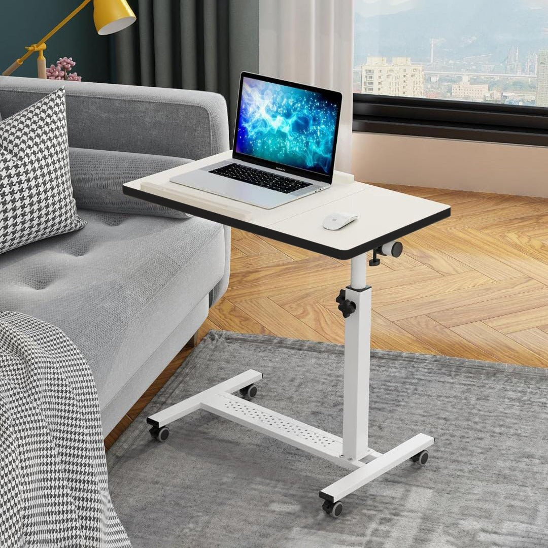 White Adjustable Overbed Laptop Stand Table with a laptop on top, positioned on the floor beside a sofa.