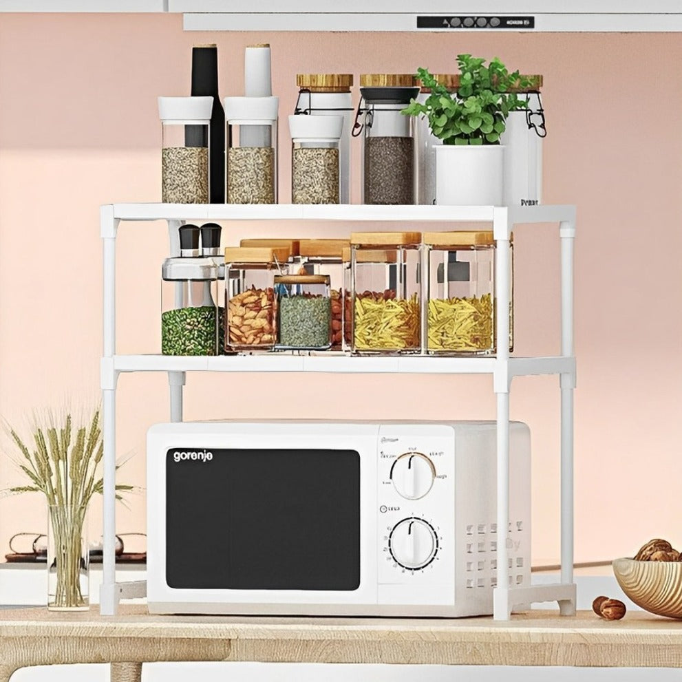 White double-layer rack organizing jars, bottles, and a microwave on a countertop.