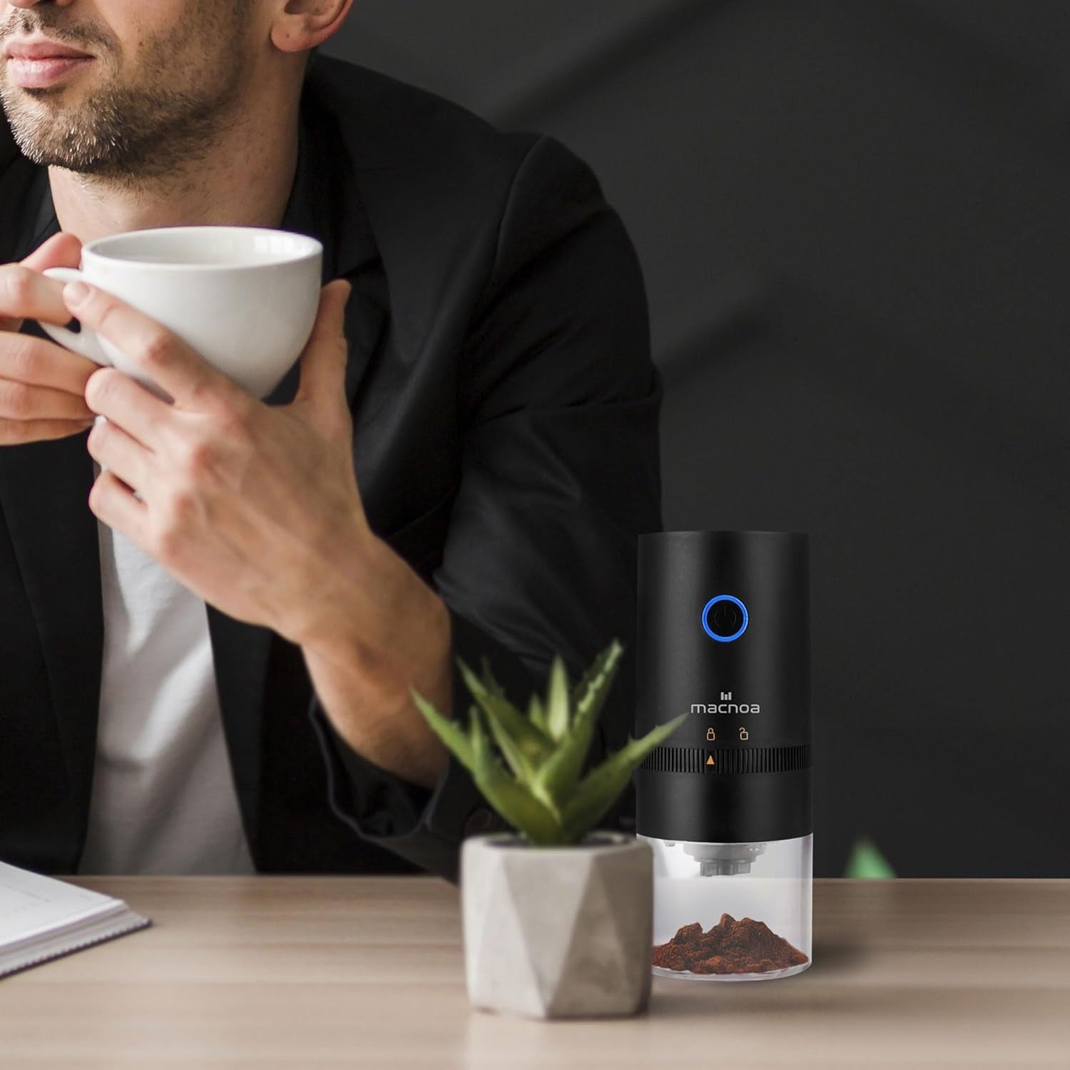 man siipin from his cup and theres Macnoa Coffee Grinder on the table