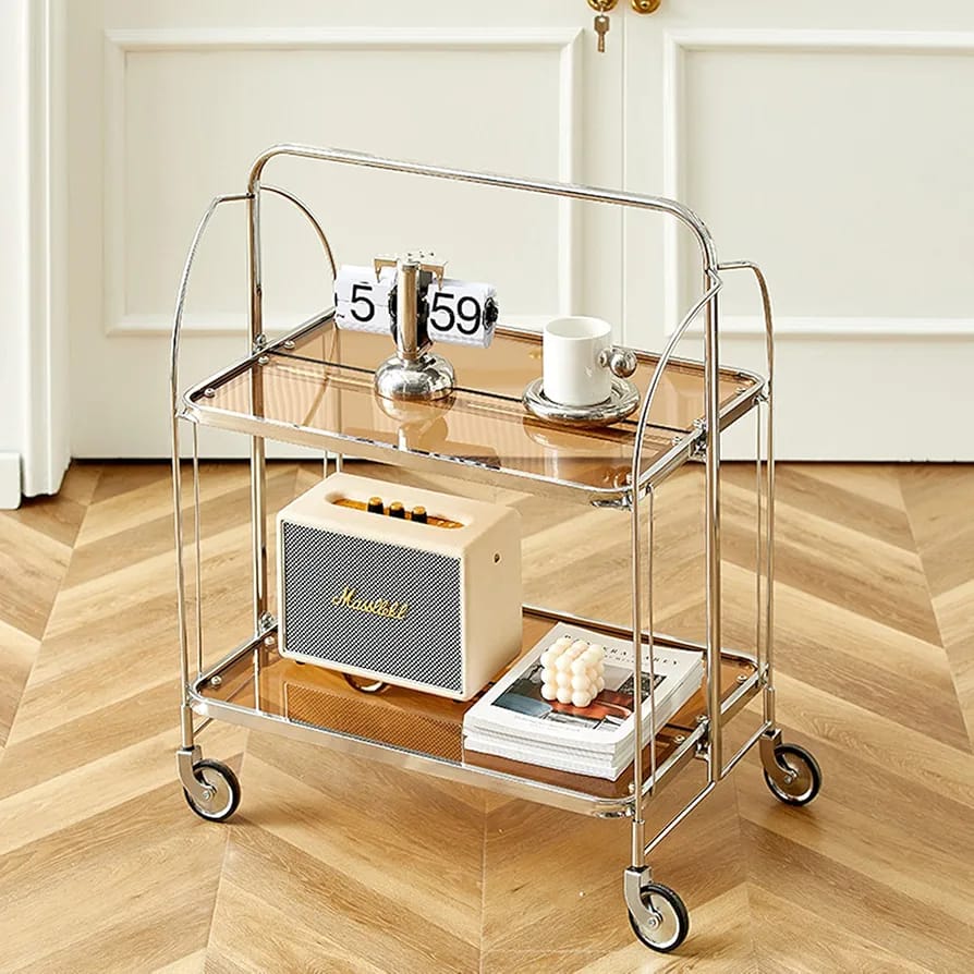 folding 2-tier serving trolley with a chrome finish, glass shelves, and rolling wheels arranged with a decor items.
