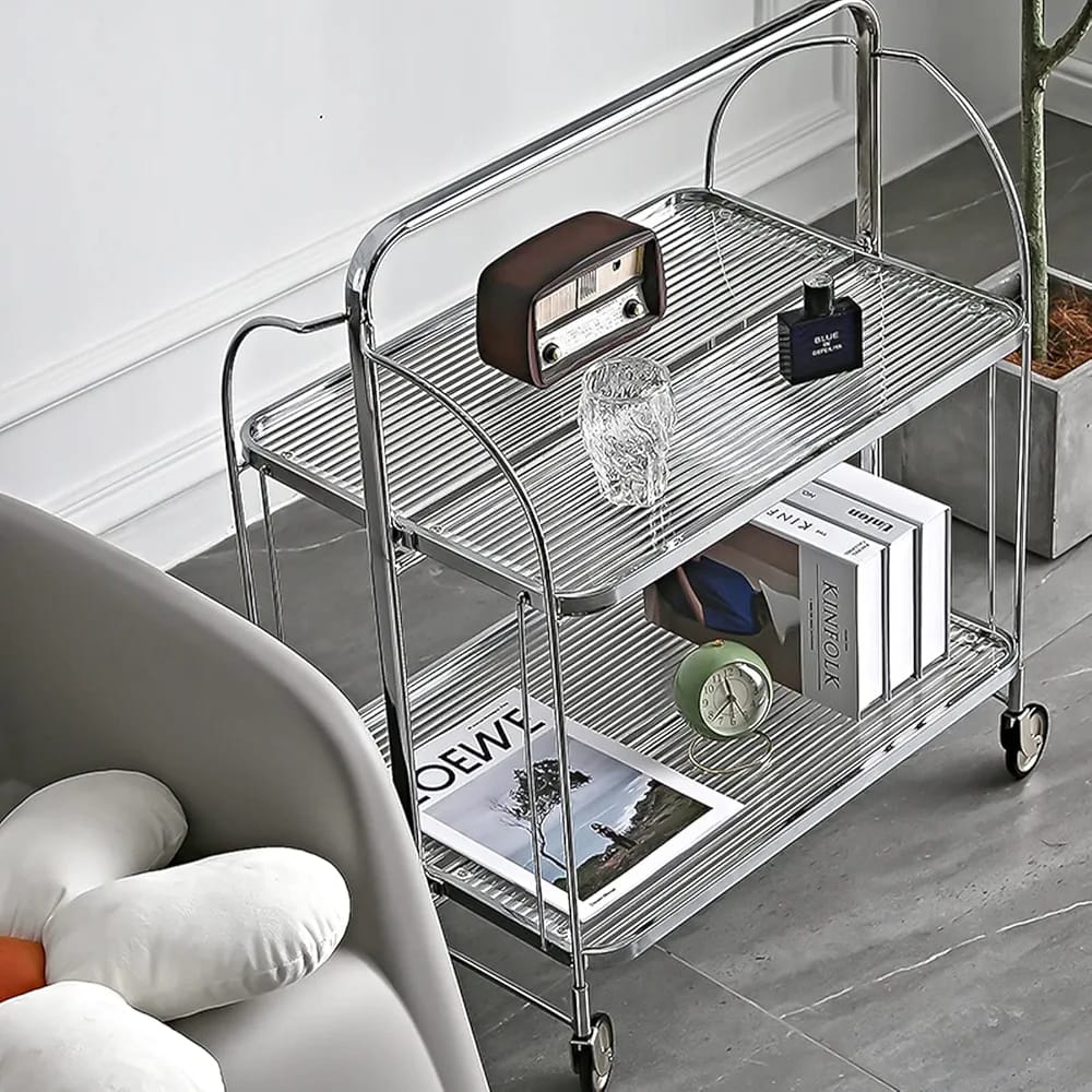 folding 2-tier serving trolley with a chrome finish, glass shelves, and rolling wheels arranged with decor items.