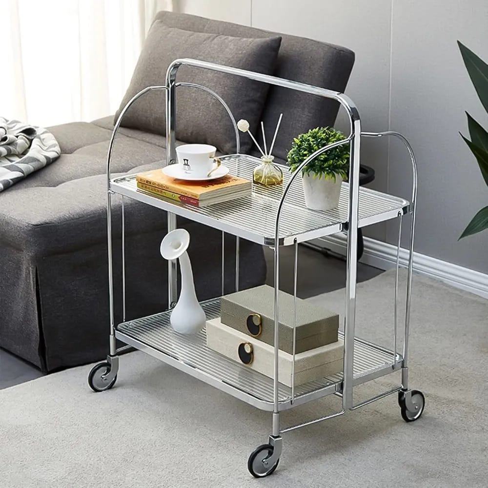 folding 2-tier serving trolley with a chrome finish, glass shelves, and rolling wheels arranged with decor items.