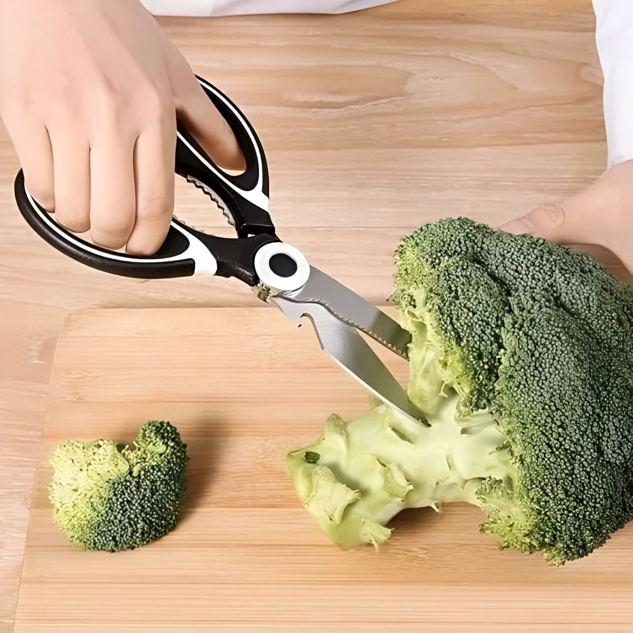 A person cutting broccoli using multi-purpose kitchen scissors on a wooden cutting board.