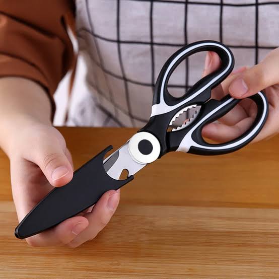 A person holding a pair of multi-functional kitchen scissors with a protective blade cover