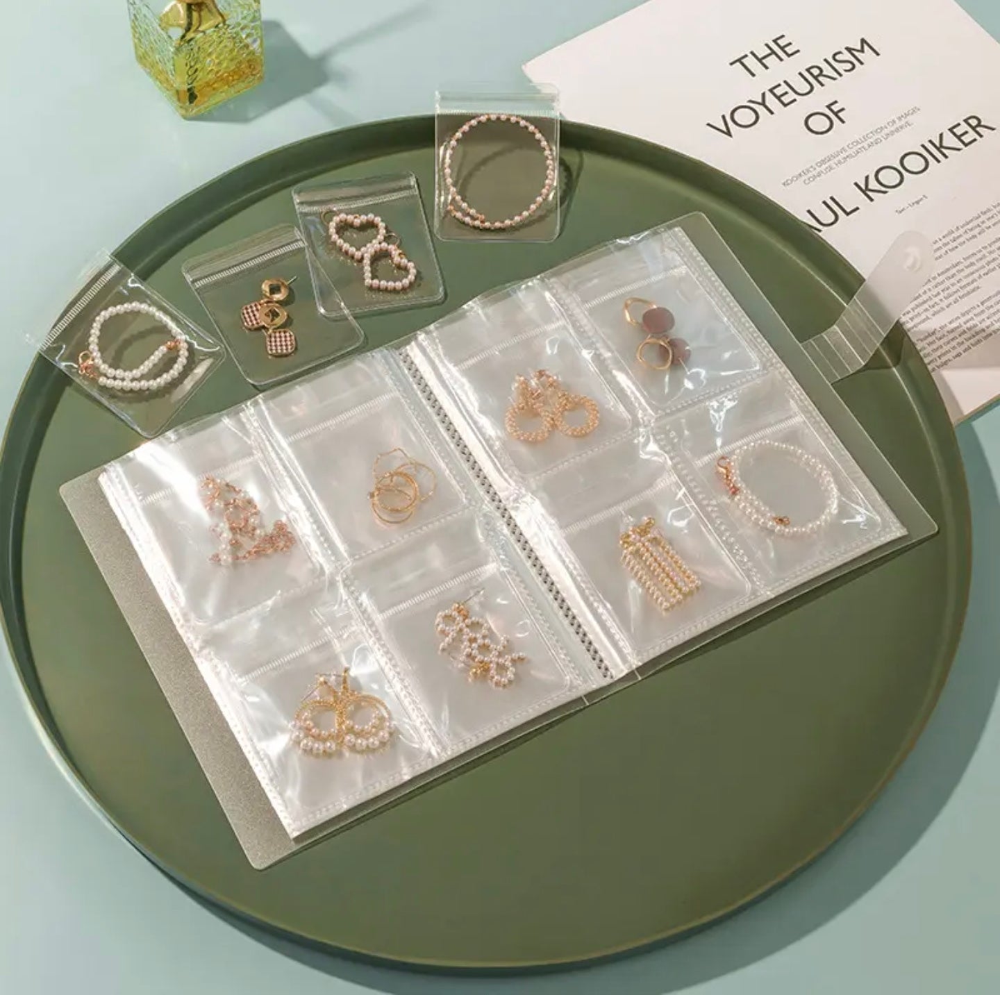 A transparent jewelry storage book with multiple clear pocket sleeves displaying neatly organized earrings, bracelets, and rings.