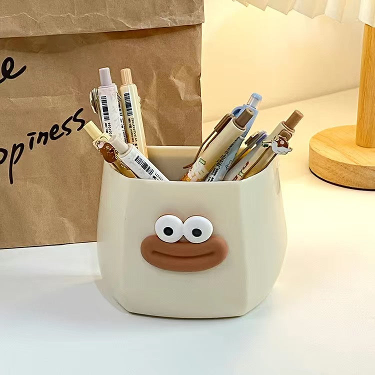 Cute cartoon-style desk organizers with smiling faces, used to hold pens, stationery, and small items.