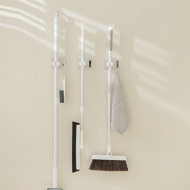 A set of wall-mounted mop and broom holders neatly organizing cleaning tools, featuring strong adhesive mounts and clips to keep items securely in place and save floor space.