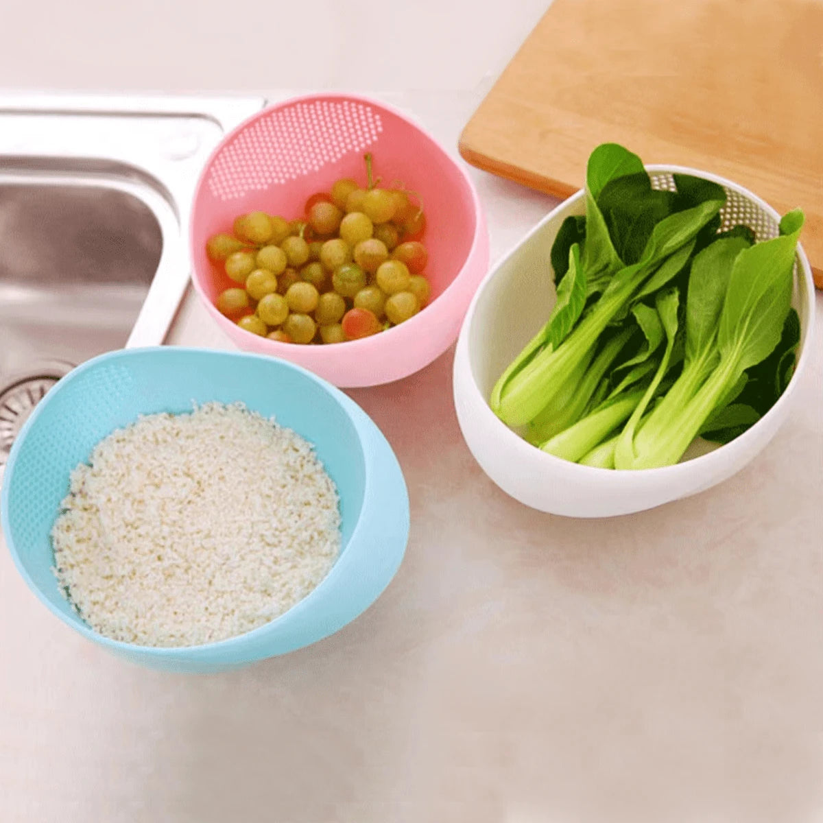 Three Plastic Rice Washing Strainer Baskets in three different colors with fruits,vegetable and rice in it placed on a counter top of kitchen 