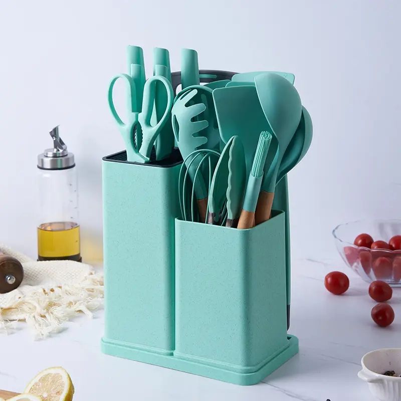18-piece silicone kitchenware set in a holder including spatulas, ladle, tongs, whisk, pasta server, brushes, and scissors, neatly organized on a kitchen countertop.