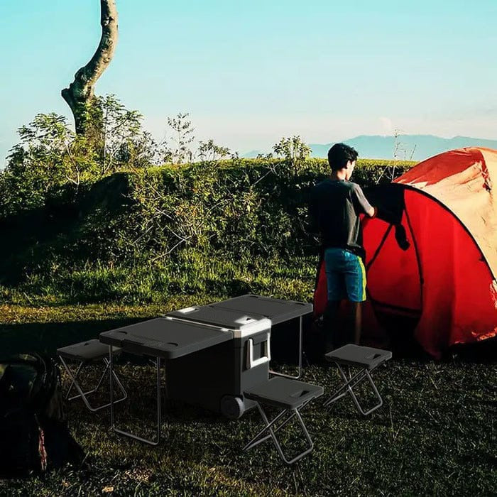 A Person is Setting Up His Tent and 32L Cooler Box With Table And Chairs are Kept Nearby.