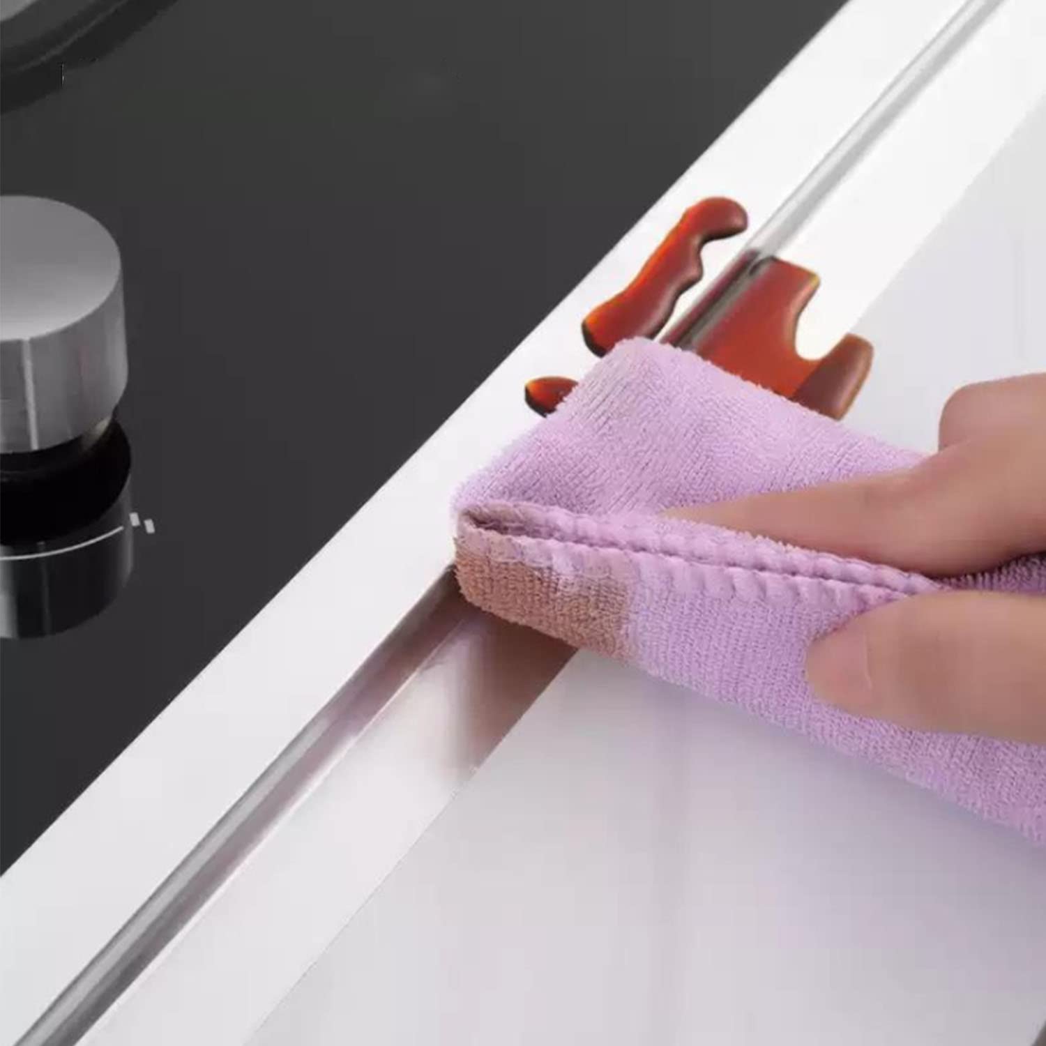 A person easily wiping off oil from a Leakproof Aluminum Foil Tape sticked beside of gas stove on a counter top 