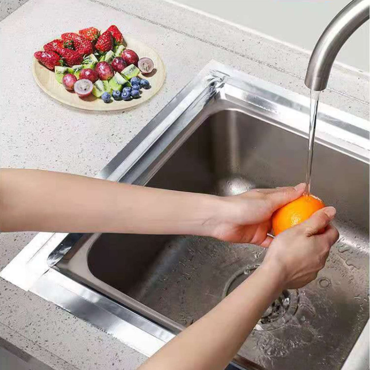 A person washing an orange in a kitchen sink on which Leakproof Aluminum Foil Tape is sticked to stop splashing of water 
