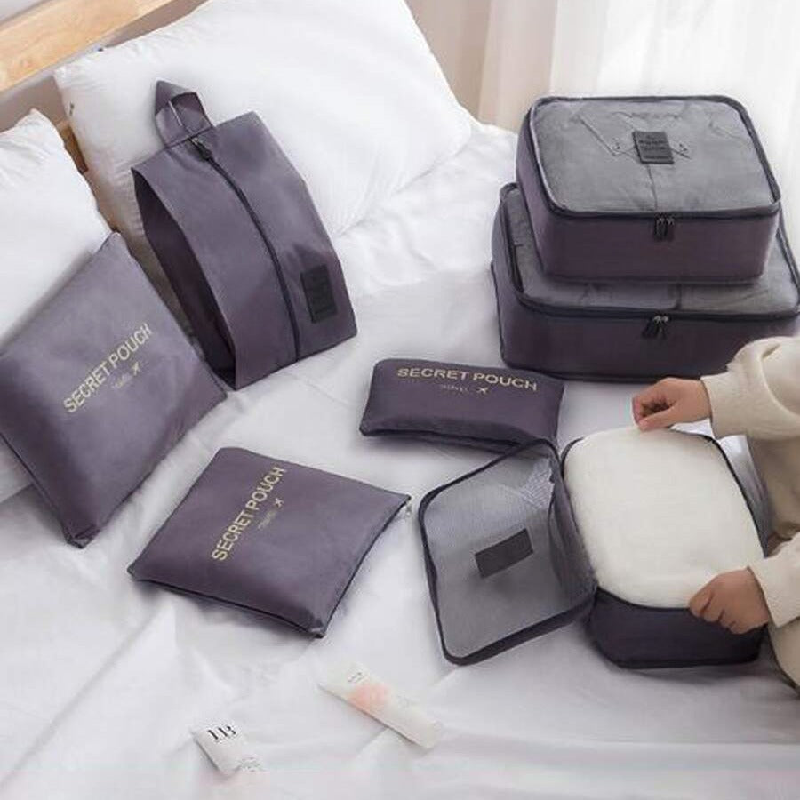 7 Pcs Travel Organizer Bags Packing Cubes Set and pouches on a bed with a hand reaching for one.