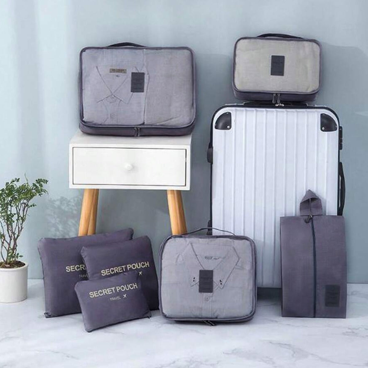 Set of gray packing cubes and a suitcase on a light-colored floor with a plant in the background.