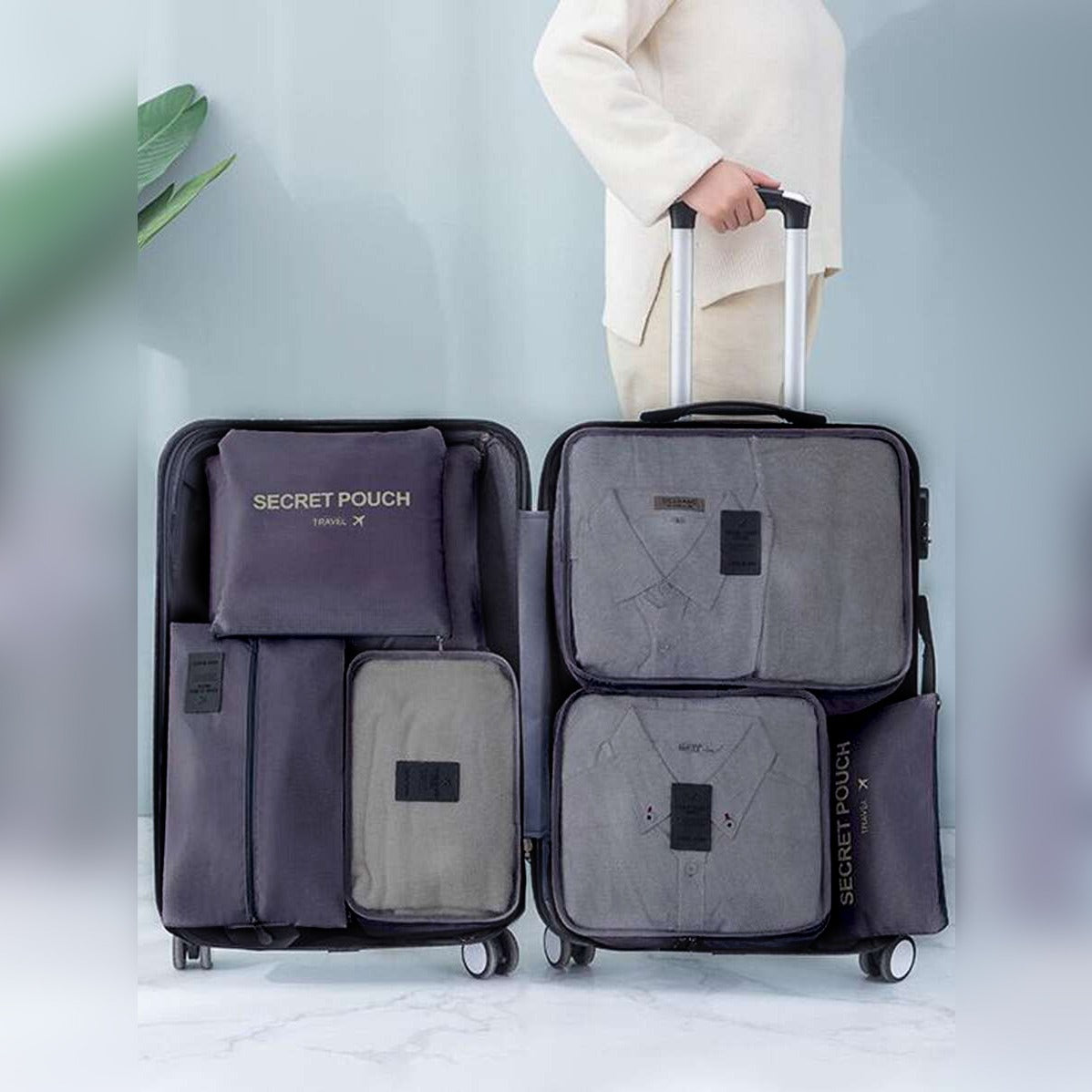 Person holding a suitcase with travel packing cubes labeled 'SECRET POUCH' on a light background.