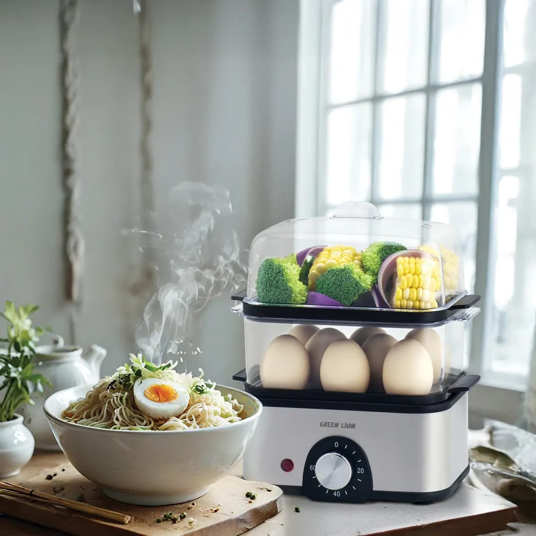 A 3-tier electric egg cooker and vegetable steamer with stacked transparent trays holding eggs, corn, and vegetables.