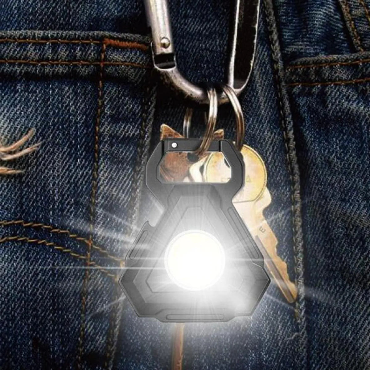 A COB rechargeable keychain pocket light, emitting a bright white light, is clipped onto a blue jeans with a carabiner.