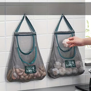 A hanging mesh storage bag with multiple compartments Stored with Vegetables and person is picking from it.