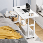 White adjustable desk next to a bed with a laptop on it