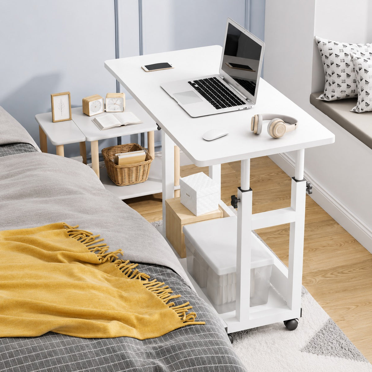 White adjustable desk next to a bed with a laptop on it
