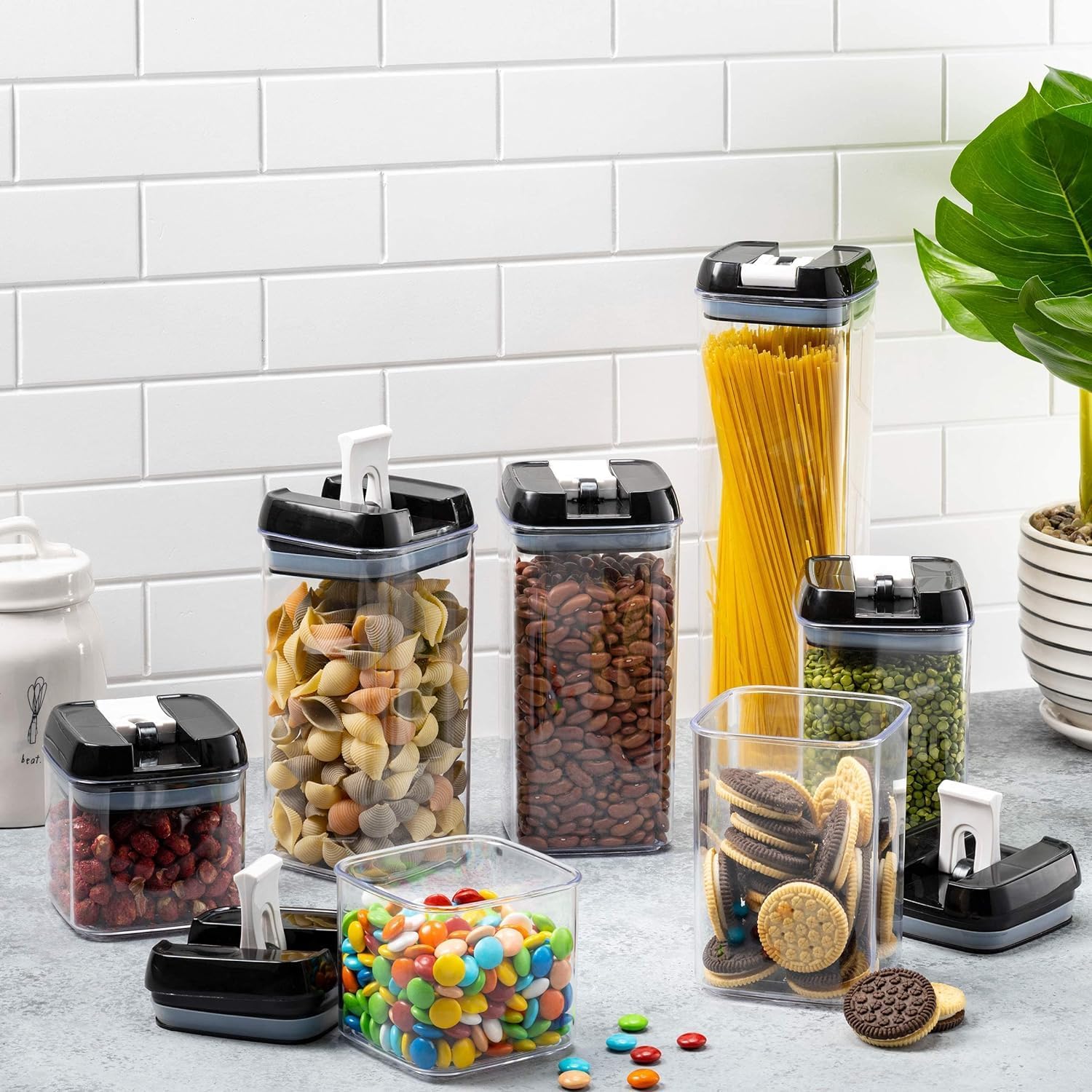 Set of clear kitchen storage containers with black lids on a countertop.