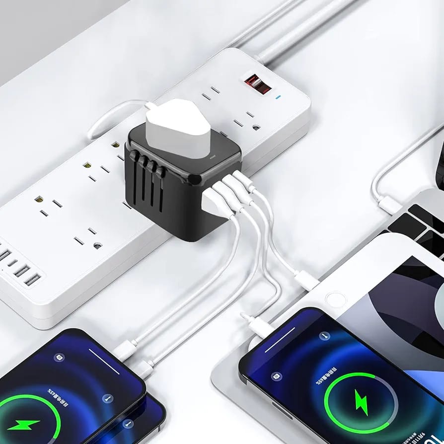 All-in-One Universal Travel Adapter with Multiple USB Ports placed on the table next to a mobile phone, which is plugged into it
