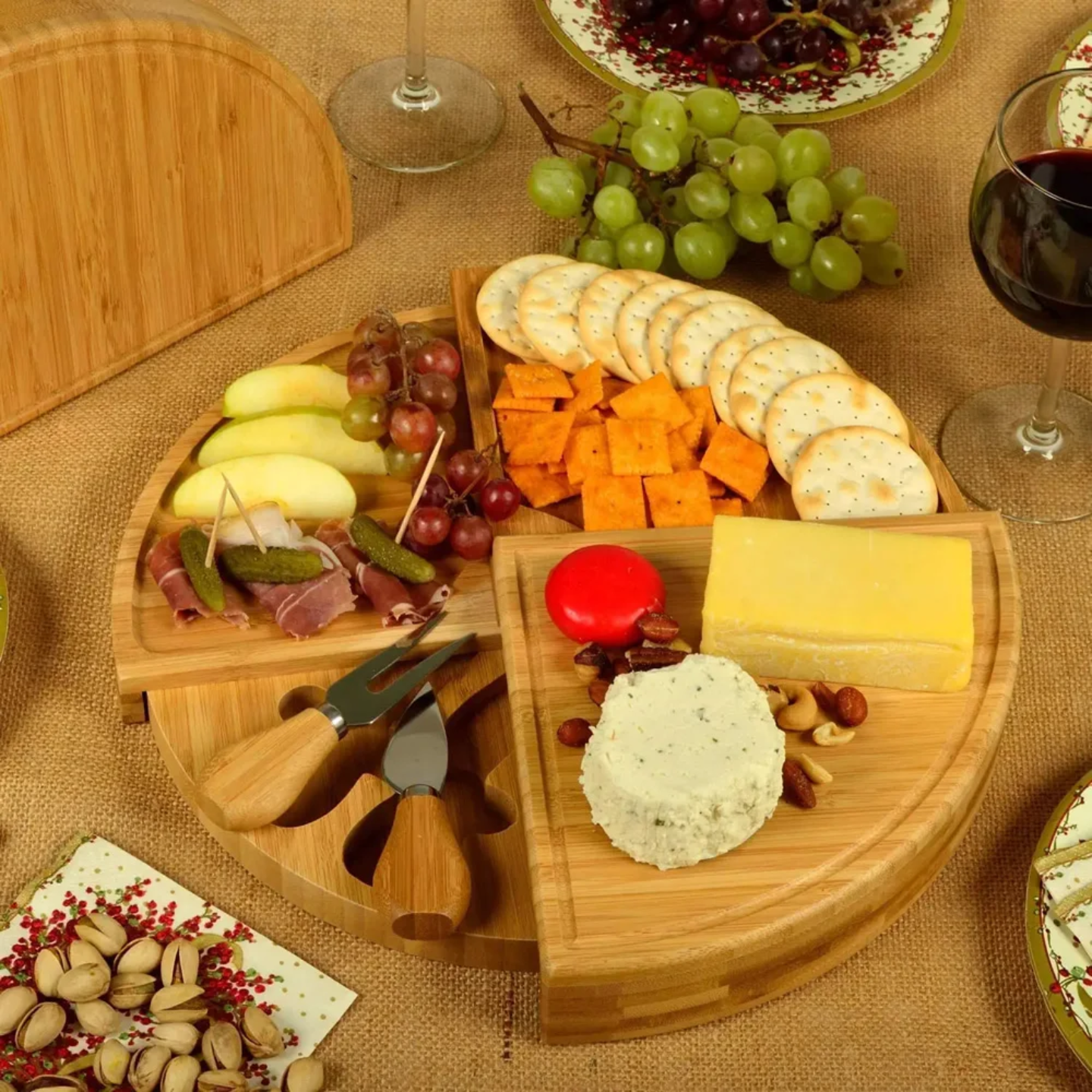 Bamboo cheese board and knife set with an assortment of cheeses, crackers, grapes, nuts.